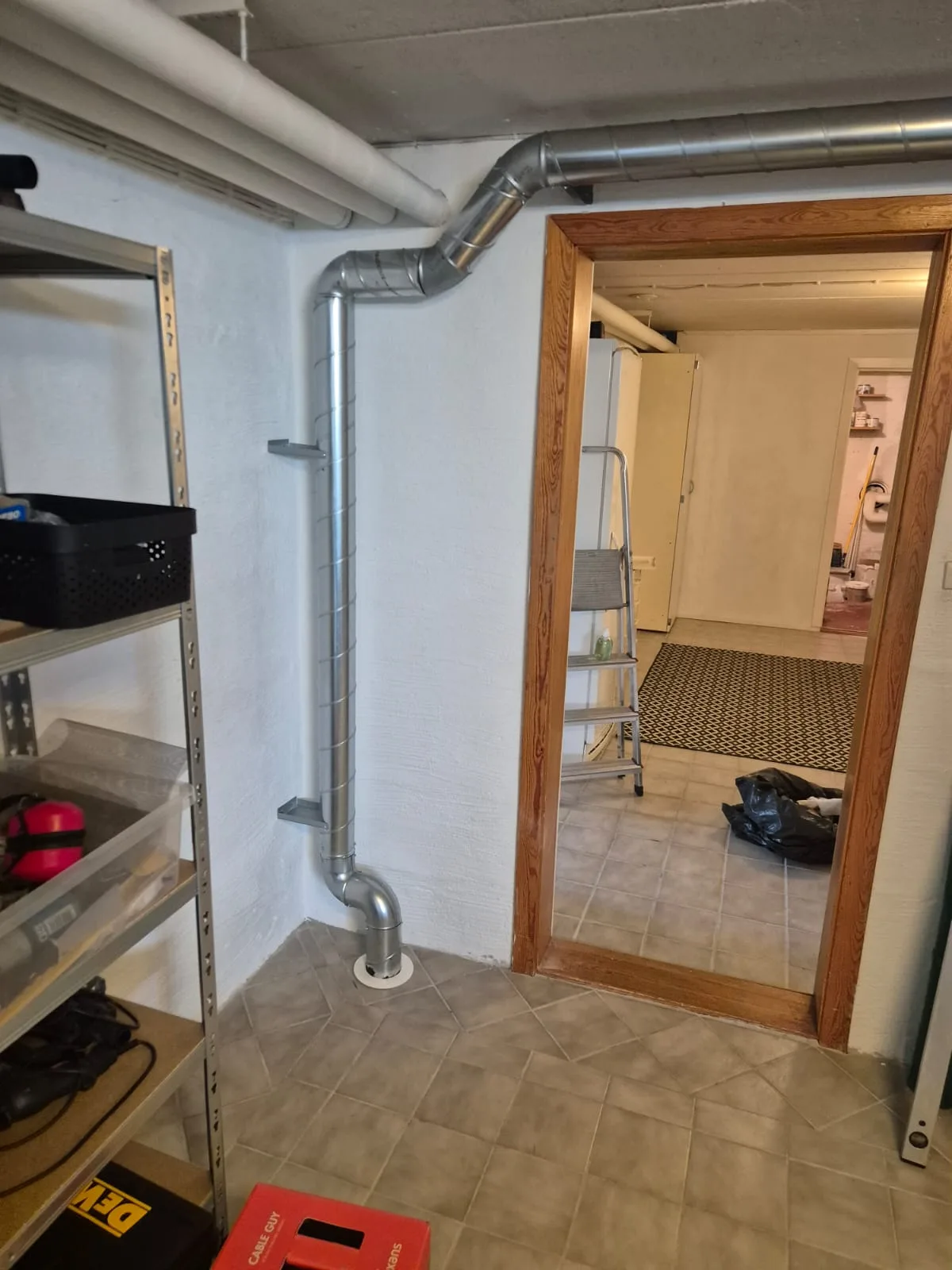 Blank ventilationskanal i en källare, dragen från en genomföring i golvet upp mot taket efter en radonmätning som visade förhöjda värden